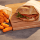 Food Huggers Fabric Bag preserving a sandwich on a wooden board next to another Food Hugger Fabric bag preserving carrot pieces