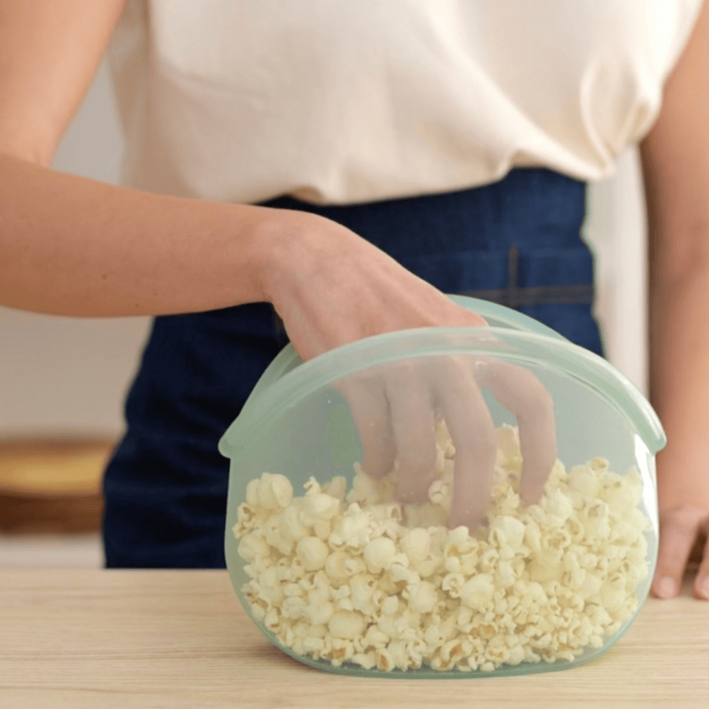 "Hand of a woman taking popcorn from a reusable Hugger bag as an alternative to plastic wrap"