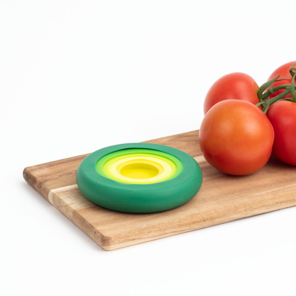 On a wooden board, tomatoes next to a set of five food huggers, the perfect alternative to plastic wrap.
