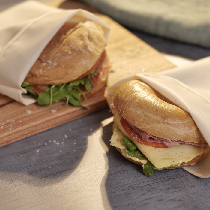 Two reusable Food Huggers fabric Bags preserving a sandwich each on top of a table