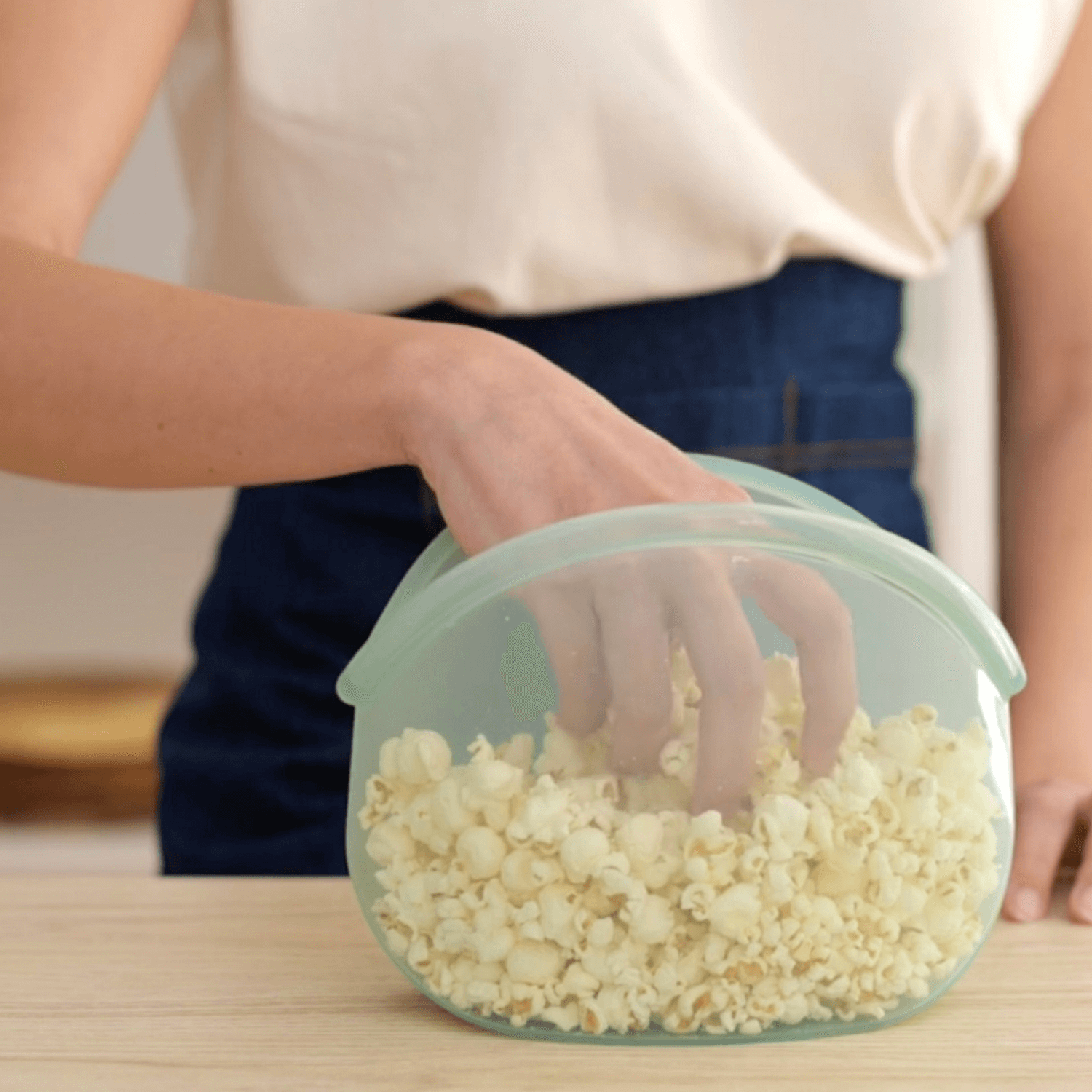 "Hand of a woman taking popcorn from a reusable Hugger bag as an alternative to plastic wrap"