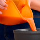 "Person pouring an orange liquid from a hugger lid into a bowl"
