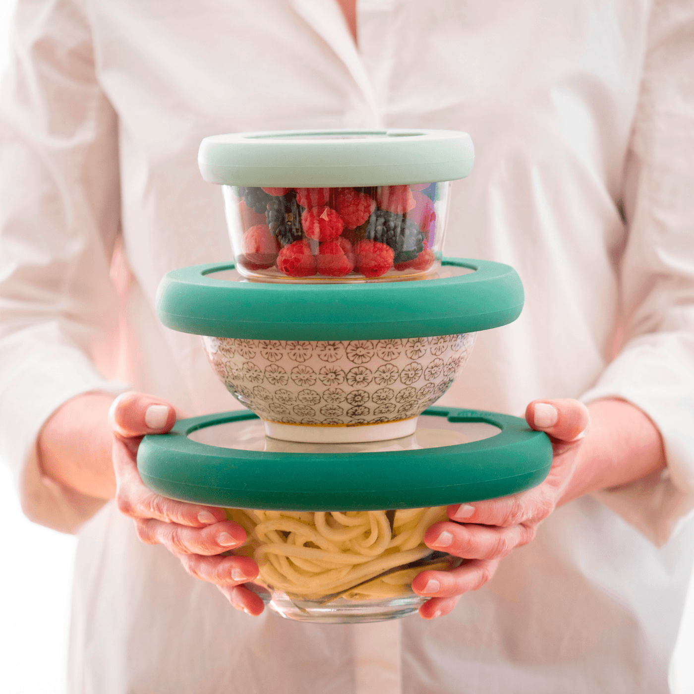 Woman holding three glass bowls with reusable lids preserving food for sustainable kitchen