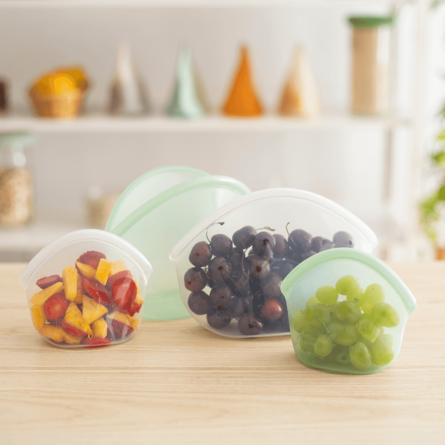 Four BPA free silicone bags on a table, three contain fruit and one is empty 