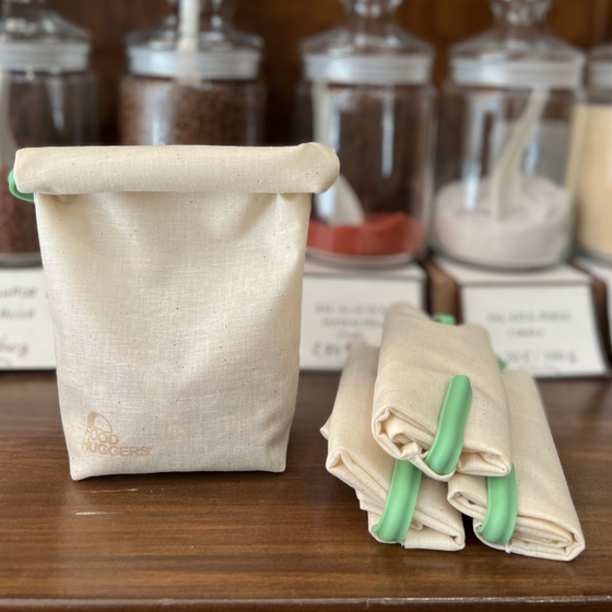 A fabric coffee bag as a reusable alternative to plastic wrap sits on a wooden table next to three other rolled up bags
